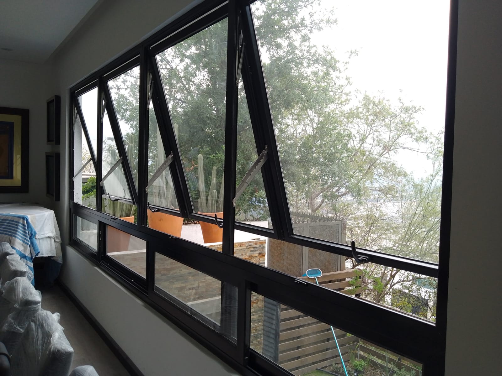 Ventanas tipo taquilla de proyección en aluminio negro con cristal claro, abiertas hacia el exterior, con corrediza inferior integrada en pasillo interior.