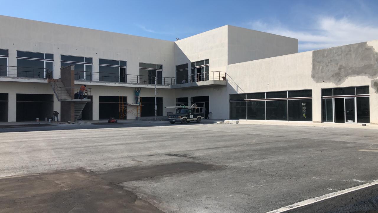 Vista panorámica de la plaza comercial con cancelería de aluminio y cristal en planta baja y alta, fachada de dos niveles con locales en obra.