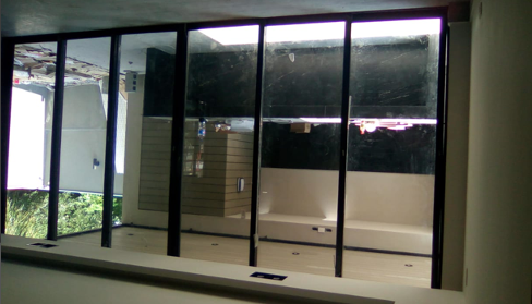 Ventanal interior de cinco paneles fijos en aluminio negro con cristal claro de piso a techo, abriendo vista panorámica al jardín.