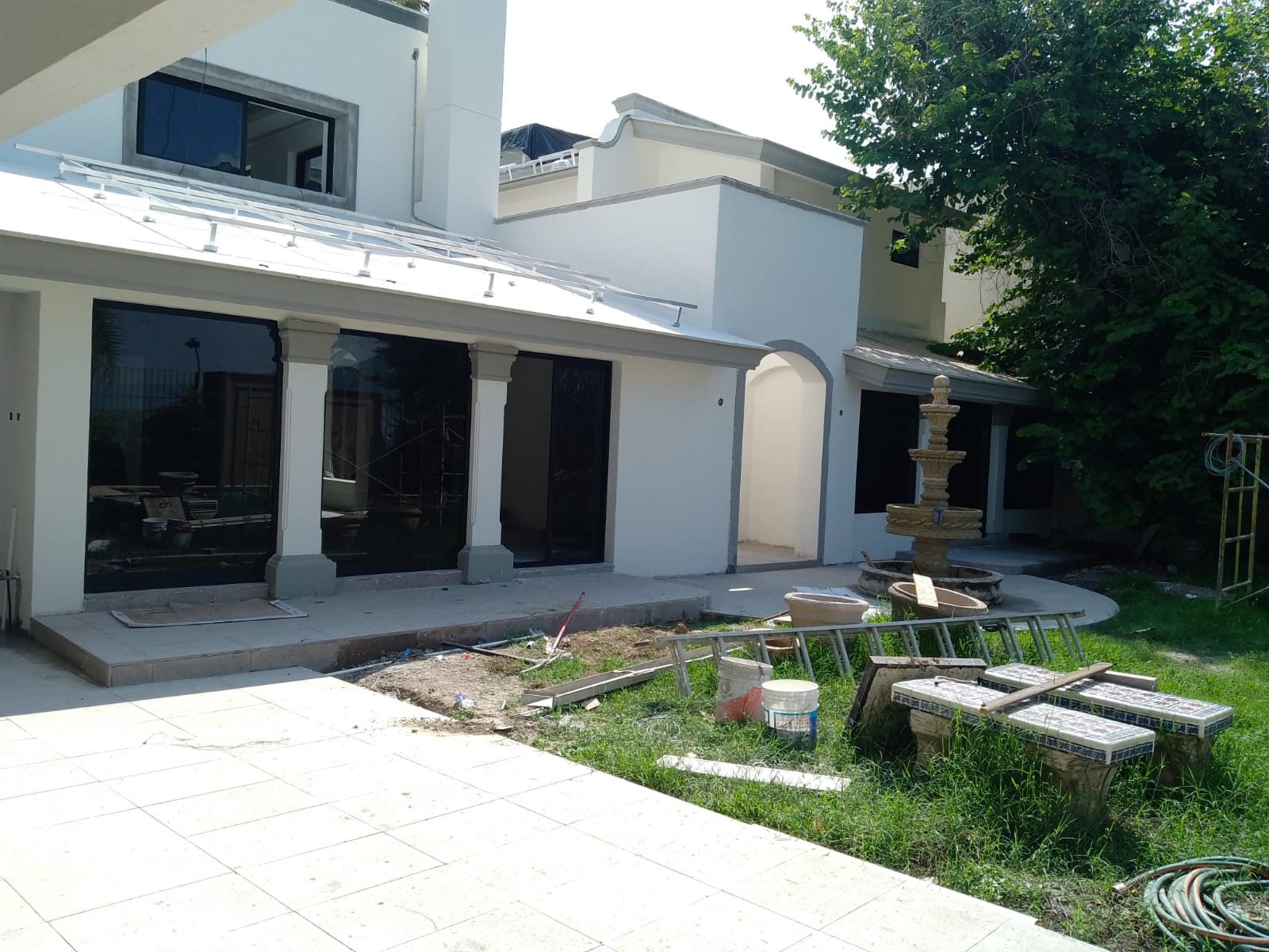 Fachada posterior con ventanería de aluminio negro y cristal reflectivo, puertas corredizas de gran formato y ventanal de doble altura sobre terraza con fuente.
