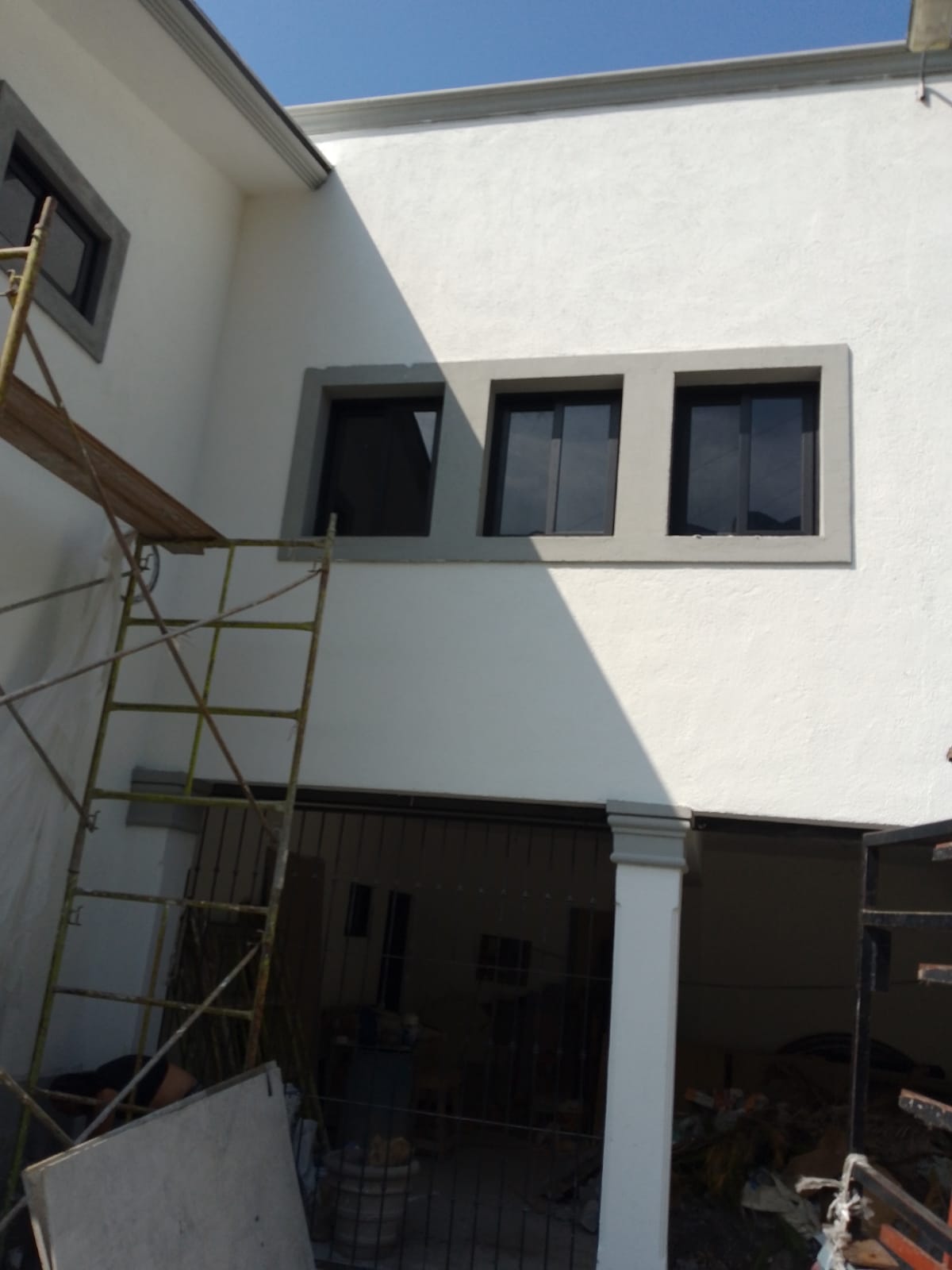 Ventanas corredizas de aluminio negro tipo taquilla en planta alta, integradas a fachada blanca con marco de cantera.