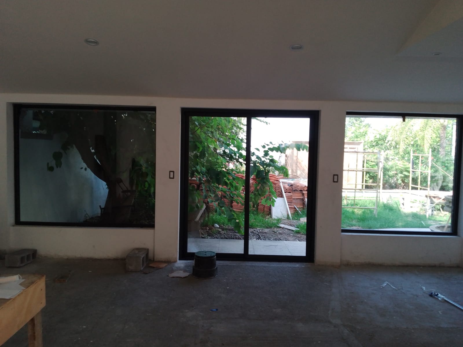 Conjunto de tres ventanales fijos y corredizos de aluminio negro con cristal claro, abriendo vista al jardín y terraza interior.