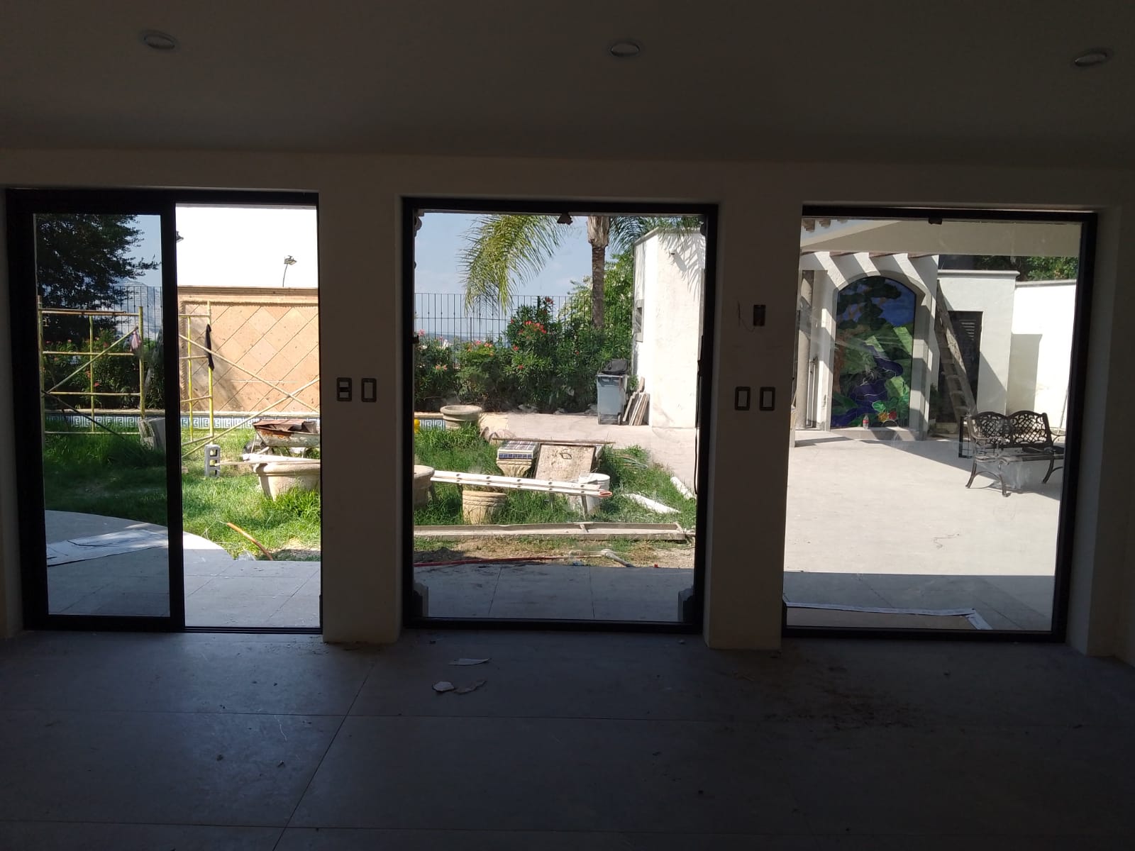 Ventanal fijo y puerta corrediza de dos hojas en aluminio negro con cristal reflectivo, integrados a pórtico con columnas blancas.