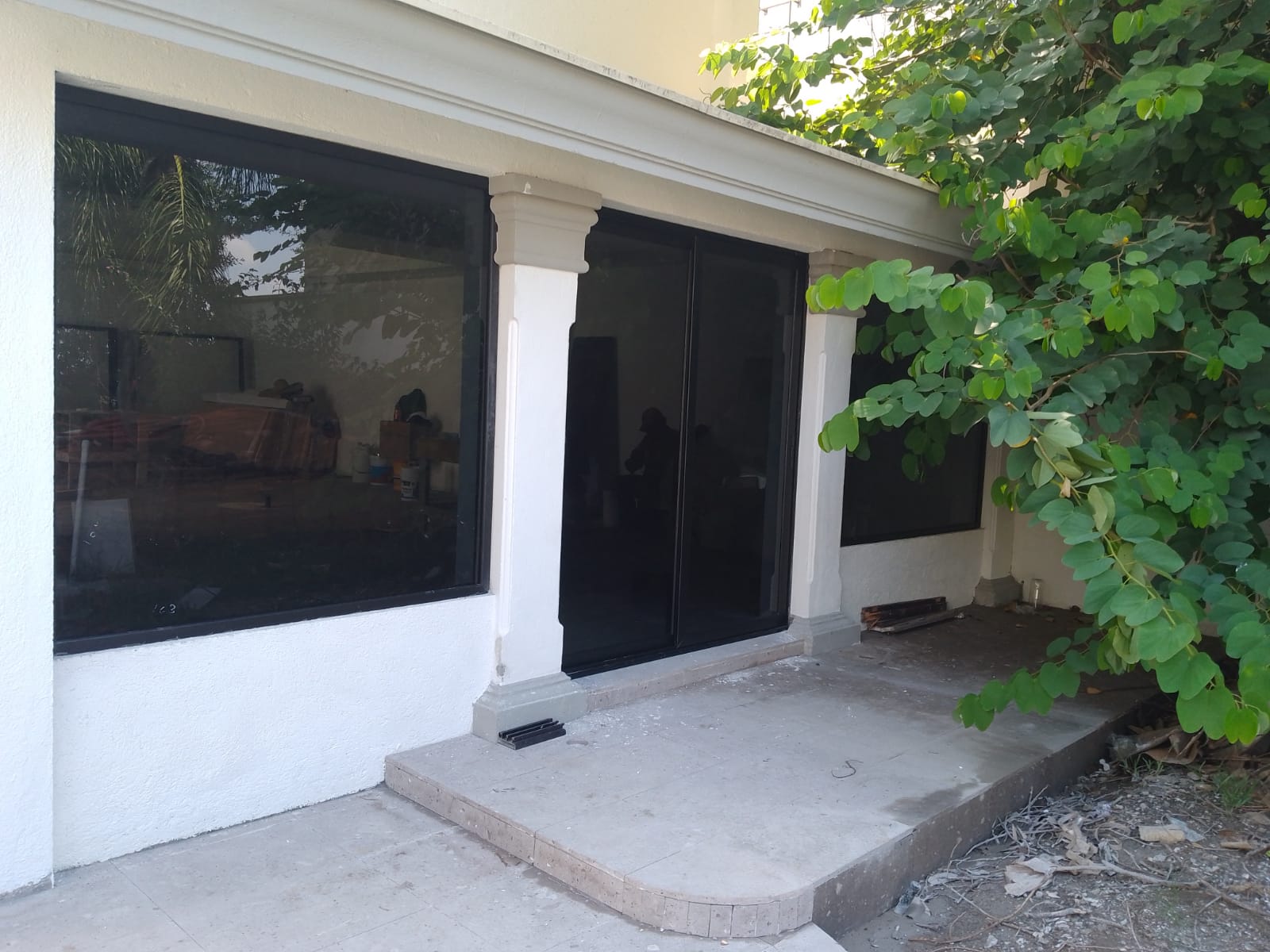Cancelería corrediza de gran formato en aluminio negro con cristal reflectivo, integrando interior con terraza cubierta y columnas.