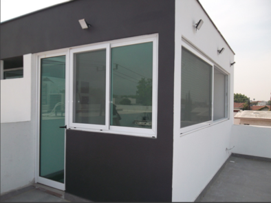 Ventana corrediza de tres hojas en aluminio blanco con cristal claro, integrada a fachada de azotea con acabado en dos tonos.