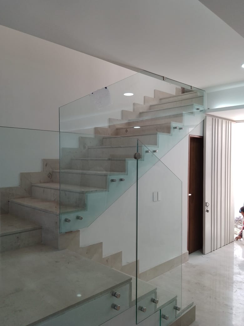 Barandal de cristal templado con herrajes de acero inoxidable sobre escalera de mármol, integrando seguridad y transparencia en doble altura.