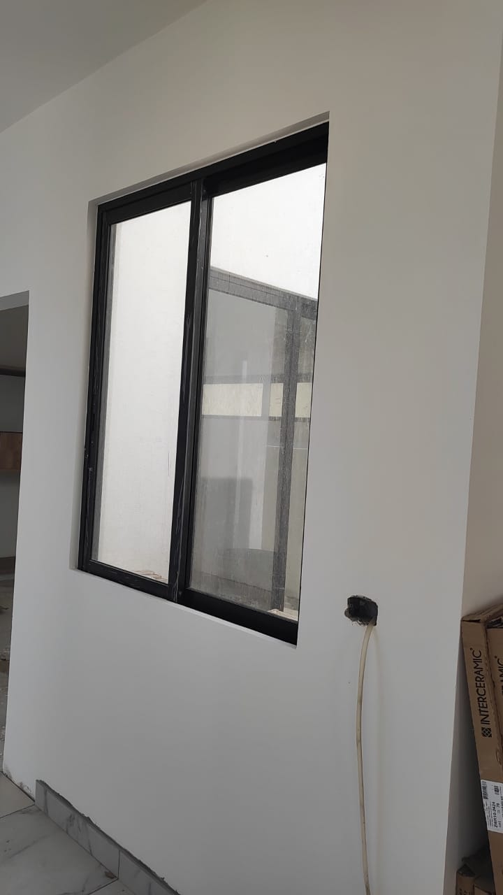 Ventana corrediza de aluminio negro con cristal claro, integrada a muro blanco con vista hacia patio interior.
