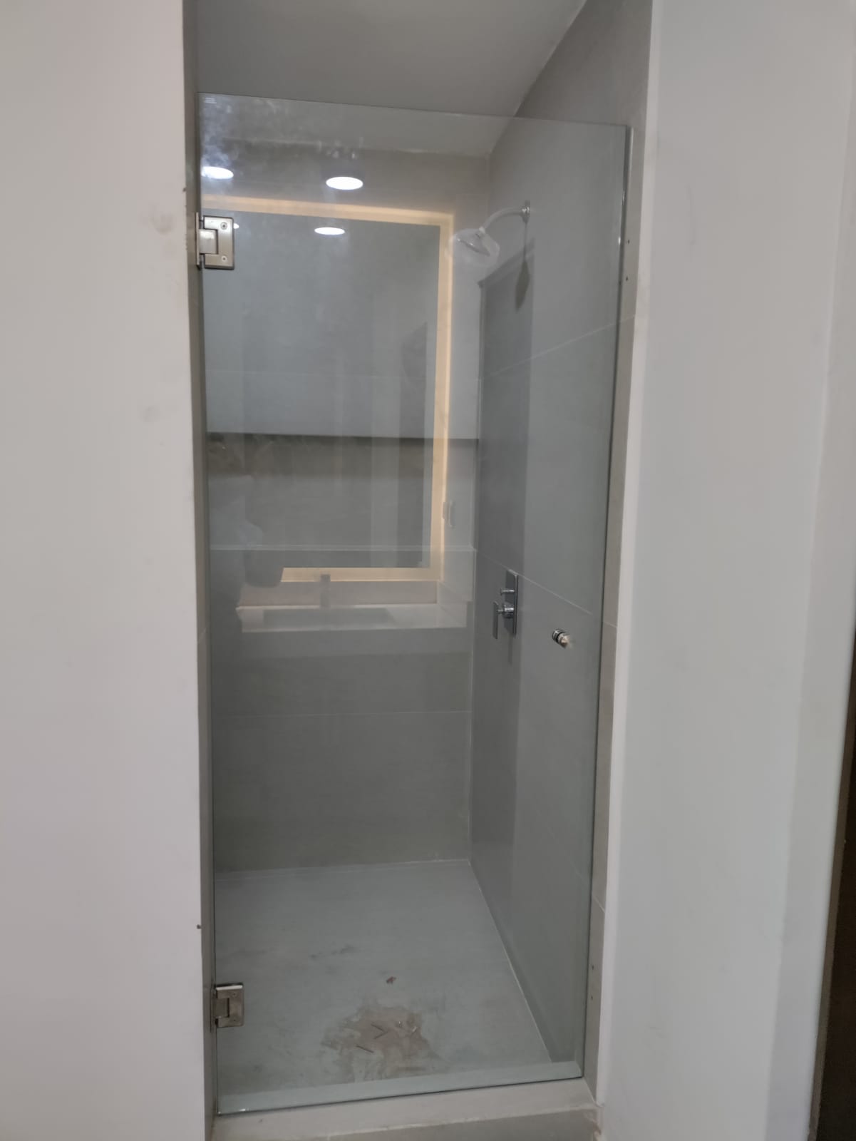 Cancel de baño abatible sin marco con bisagras de acero inoxidable, cristal templado de piso a techo en regadera privada.
