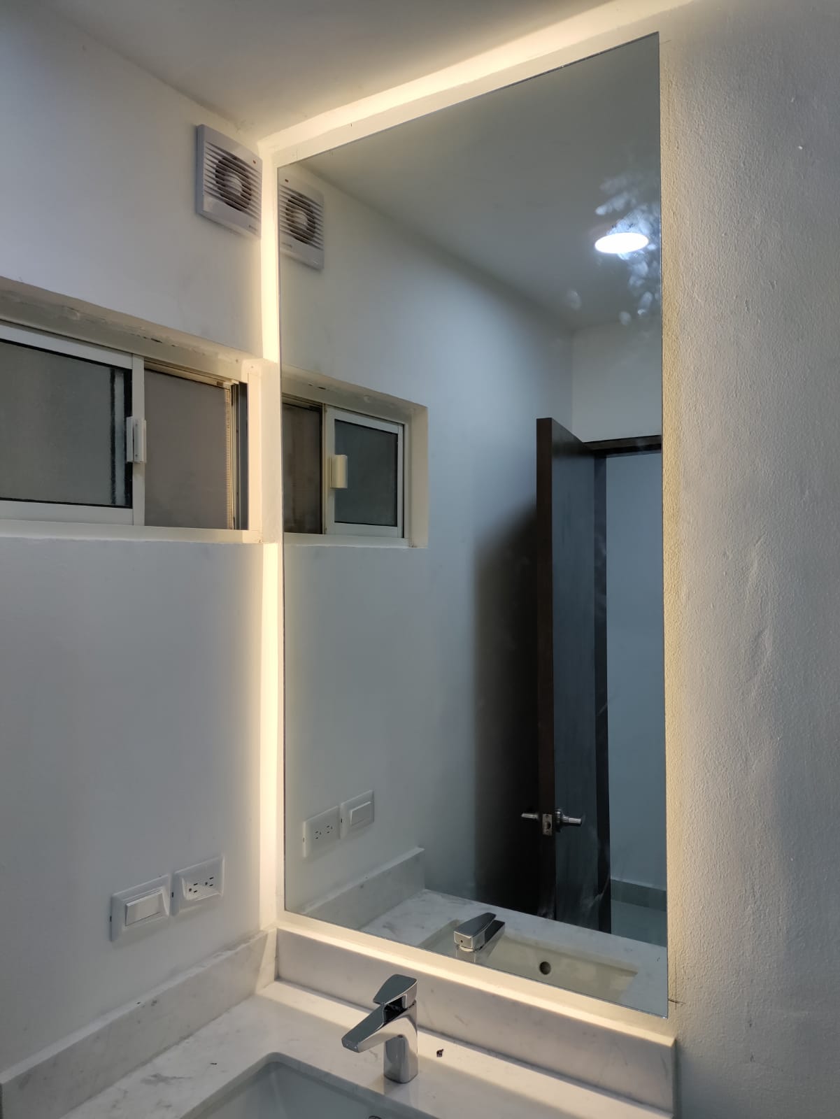 Espejo a medida con iluminación LED perimetral retroiluminada, instalado sobre cubierta de mármol en baño.