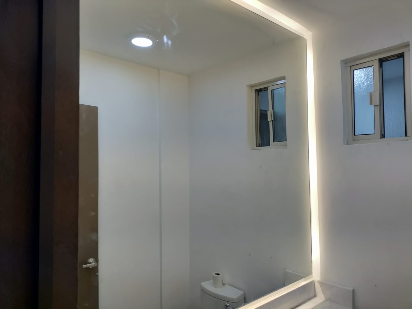 Espejo de gran formato con iluminación LED perimetral, integrado a muro de baño con acabado minimalista.