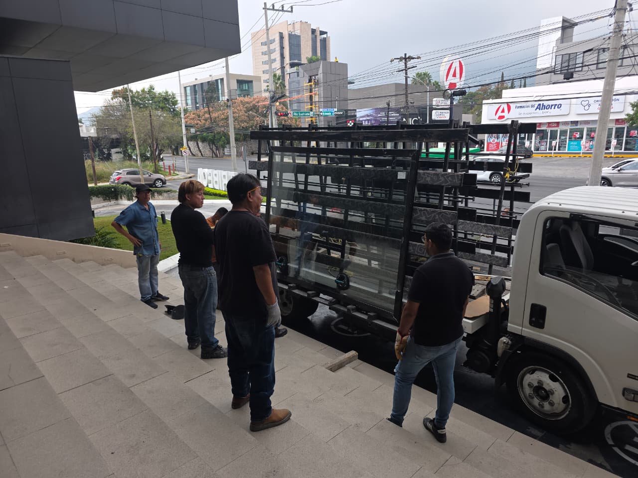 Maniobra de descarga de cancelería de aluminio negro de gran formato con cristal templado, lista para montaje en obra.