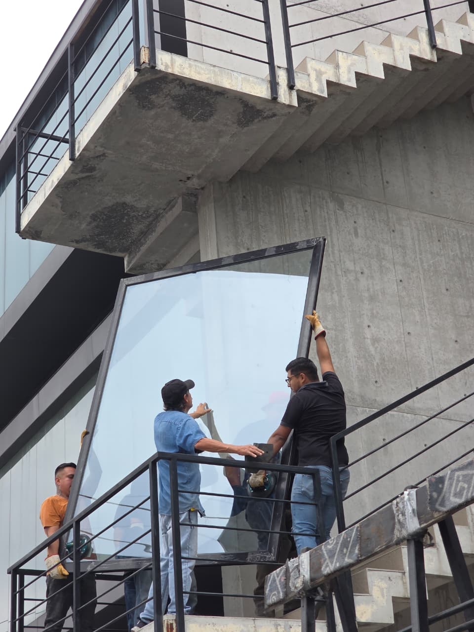 Instalación de cristal templado de gran formato bajo escalera de concreto, ajuste de perfil de aluminio negro a medida.