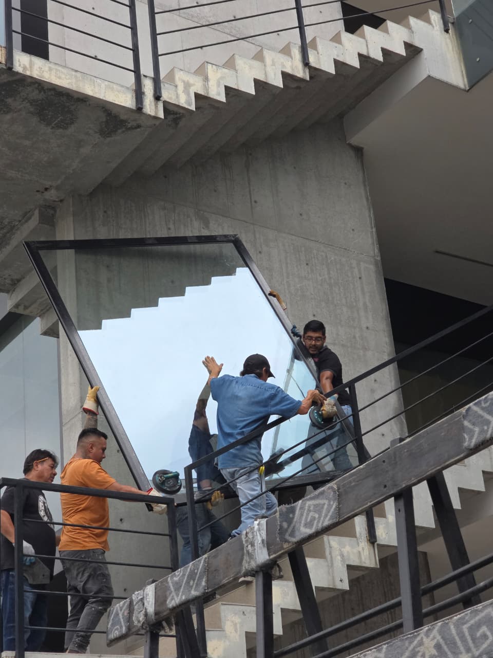 Colocación final de panel fijo de cristal templado con marco de aluminio negro en cubo de escaleras, sellado y aplomado.