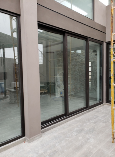 Puerta corrediza de PVC en acabado chocolate con cristal claro de gran formato, acceso a patio interior.
