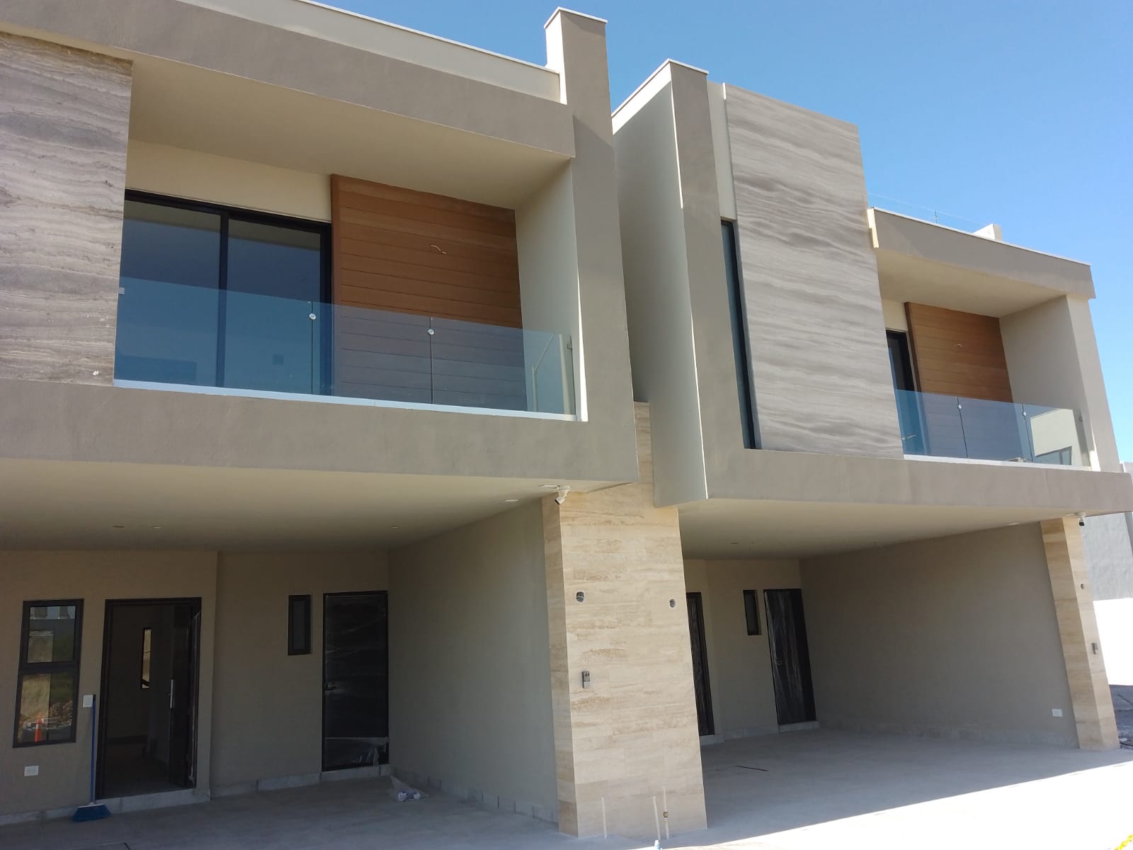 Fachada de residencias contemporáneas con barandales de cristal templado sin marco en balcones, cancelería de aluminio negro y ventanales de gran formato.