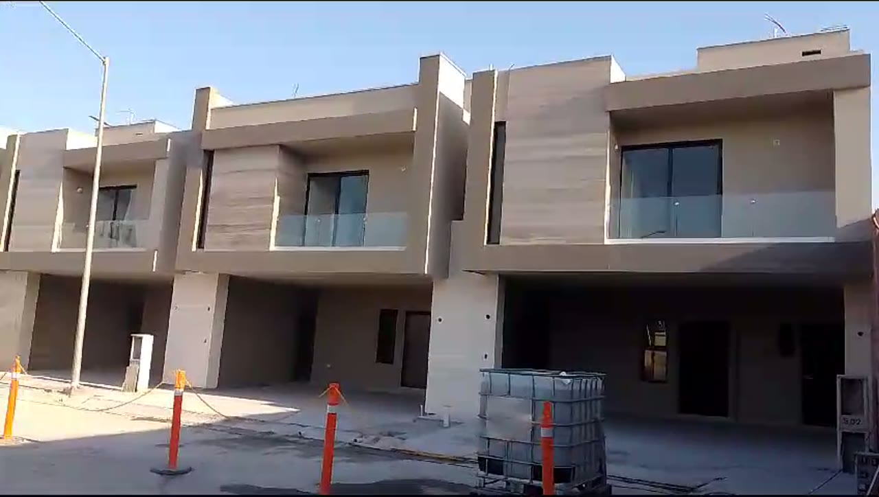 Vista del conjunto residencial con fachadas de doble altura, ventanería en aluminio negro y cristal claro.