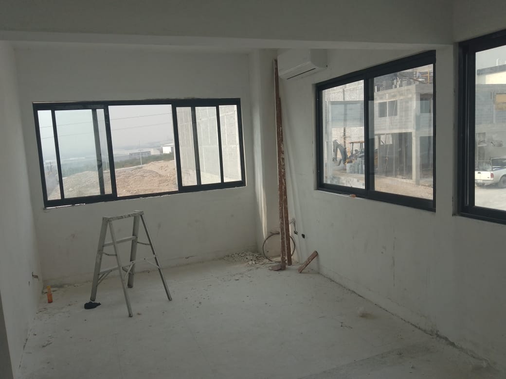Oficinas interiores de la nave industrial con ventanería corrediza de aluminio negro y cristal claro, integrando vista al exterior y al patio de maniobras.