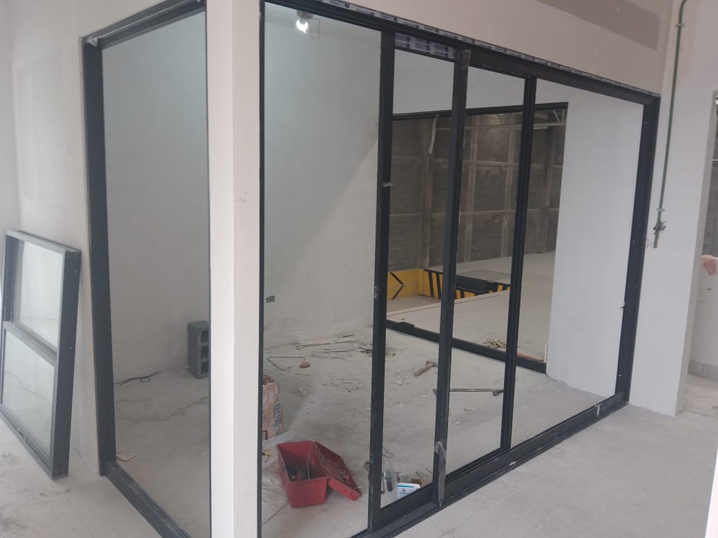 Cancelería de aluminio negro con puerta corrediza de tres paneles y cristal claro, dividiendo oficina interior del área operativa.