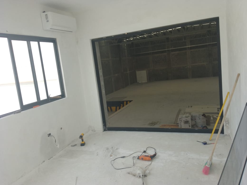 Ventanal panorámico de cinco paneles en aluminio negro con cristal claro, abriendo vista de planta alta hacia el complejo industrial.