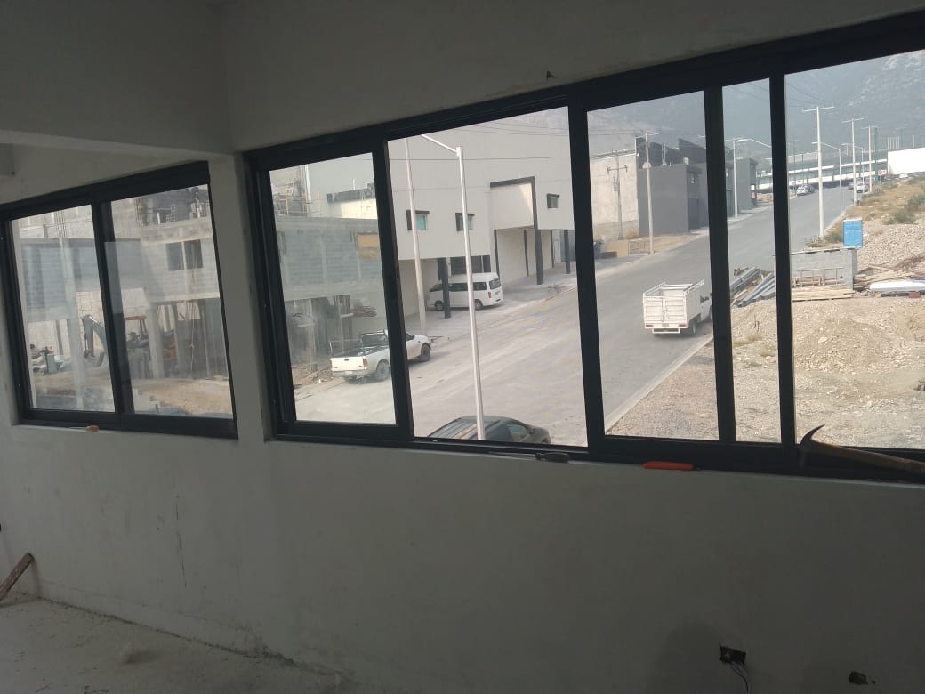 Ventanal interior de gran formato con vista hacia el área operativa de la nave, perfilería de aluminio negro y cristal claro.