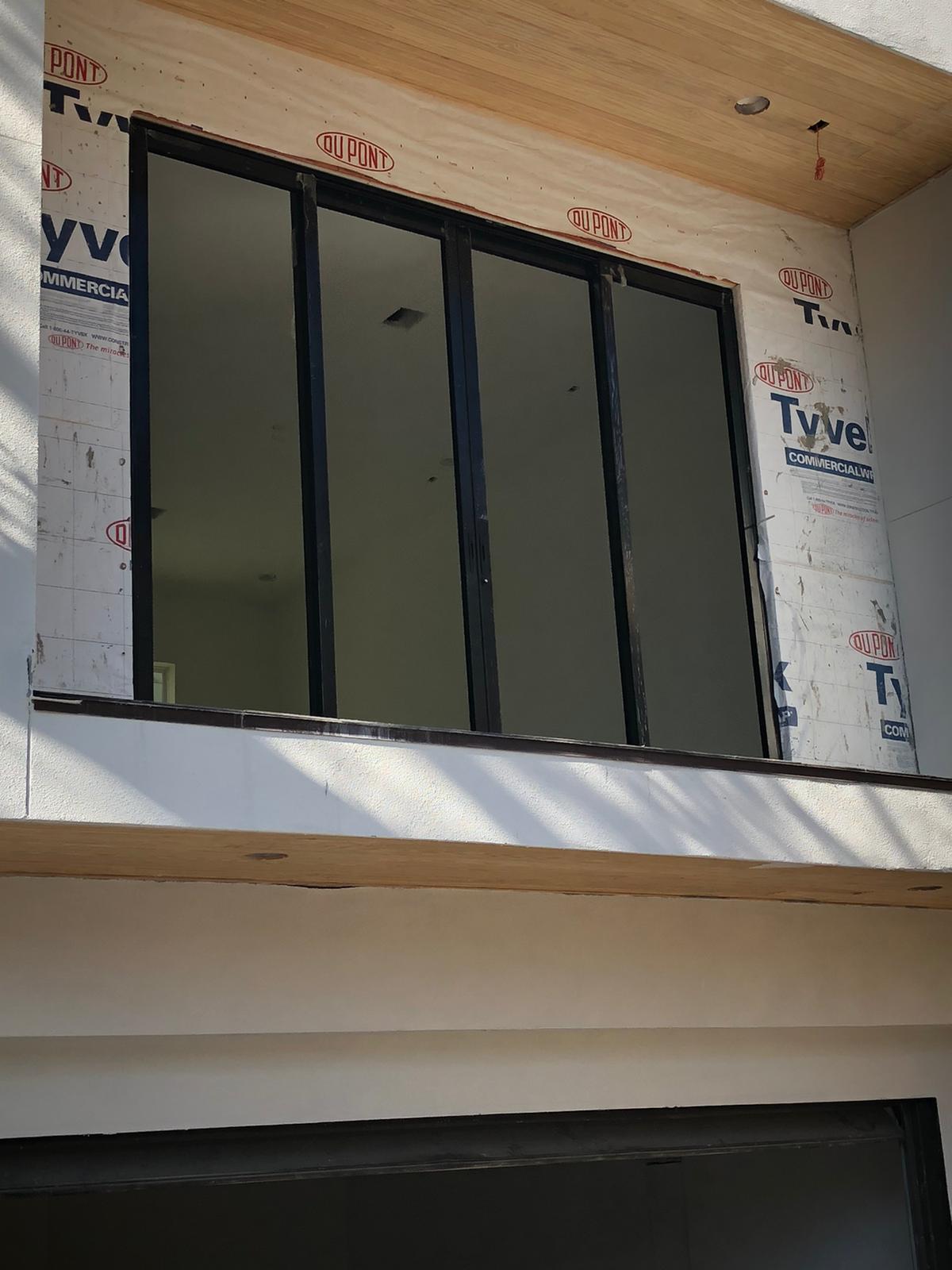 Ventana corrediza de cuatro hojas en aluminio negro con perfil reforzado para vano amplio en planta alta.