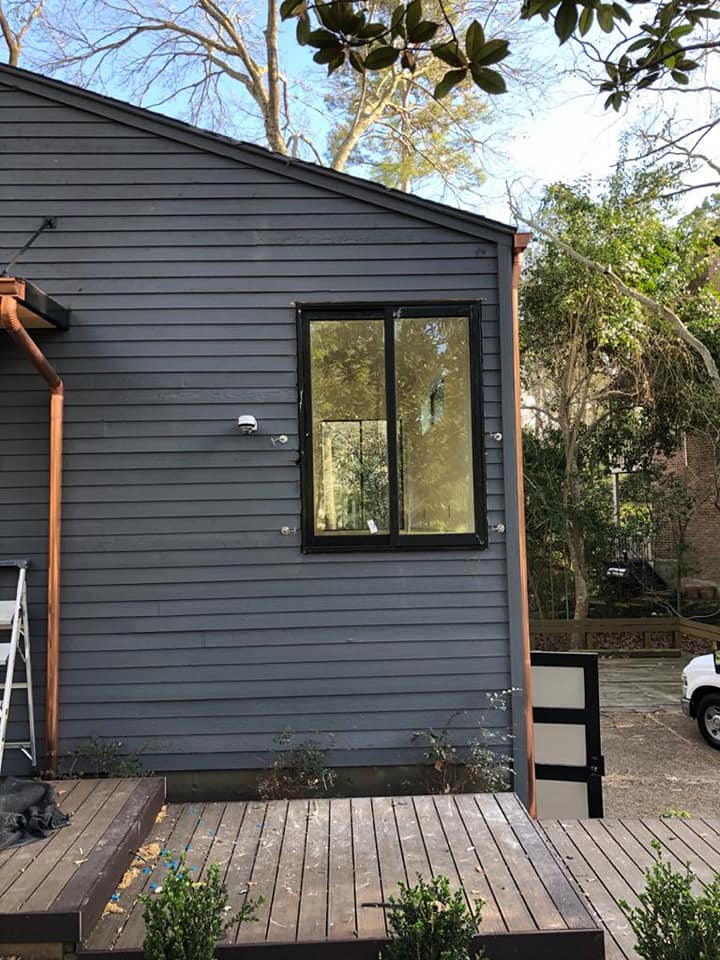 Ventana corrediza de dos hojas en aluminio negro instalada sobre fachada con revestimiento de madera horizontal.